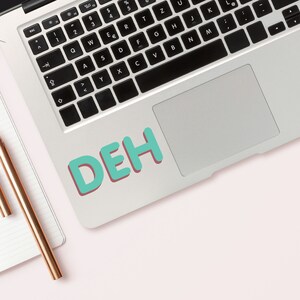 May include: A silver laptop computer with a teal blue sticker that says "DEH" on the trackpad.