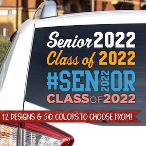 May include: A white car with a black window sticker that says "Senior 2022 Class of 2022 #Senior CLASS OF 2022". The sticker is in white, orange, blue, and pink lettering. The text below the sticker says "12 DESIGNS & 50 COLORS TO CHOOSE FROM!"