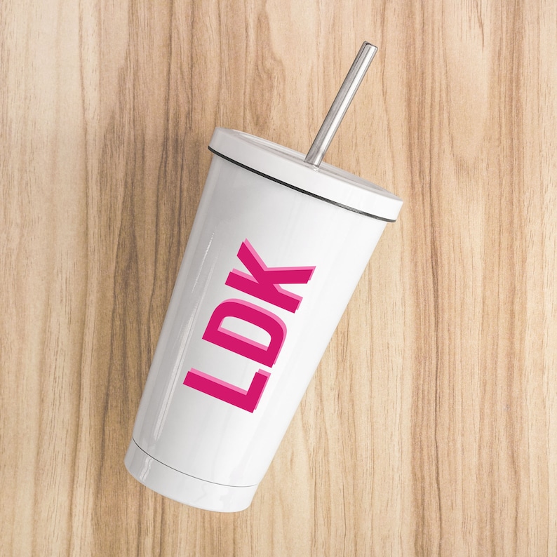 May include: White tumbler with a pink "LDK" graphic and a silver straw. The tumbler is on a wood background.