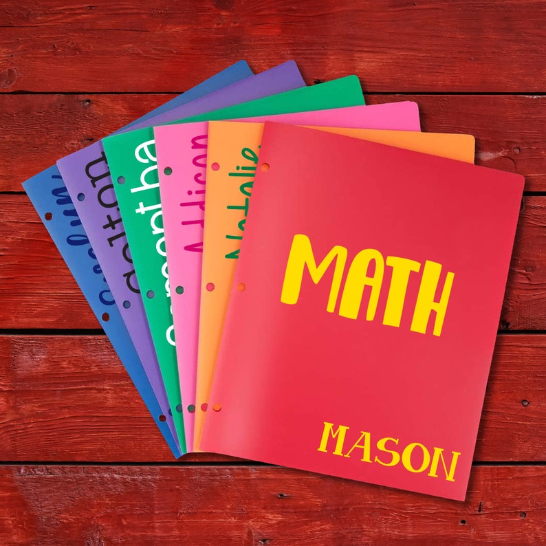 K&ouml;nnte beinhalten: Ein Stapel bunter Plastikordner mit verschiedenen F&auml;chern, darunter "Mathe" und "Mason".