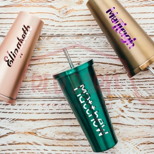 Puede incluir: Tres vasos de acero inoxidable personalizados con tapas y pajitas. Los vasos son de oro rosa, oro y verde. Los nombres "Elizabeth", "Mattiegh" y "Matthew" est&aacute;n grabados en los vasos.