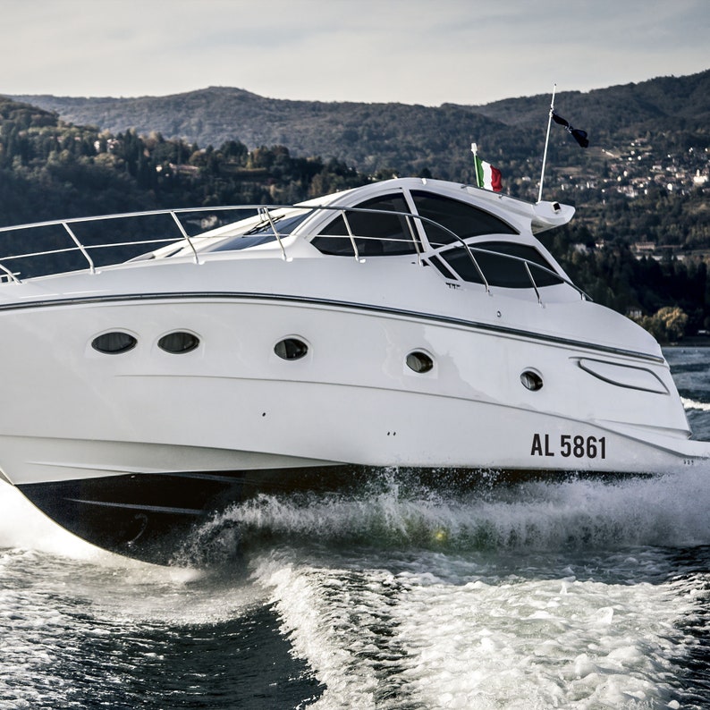 May include: A white motorboat with a black stripe and a black flag on the back. The boat is moving through the water and leaving a wake. The boat has a registration number "AL 5861" on the back.