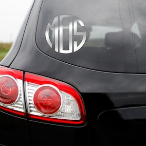 Puede incluir: Un coche negro con una pegatina de monograma plateado en la ventana trasera. La pegatina es un c&iacute;rculo con las letras "MOS" dentro.