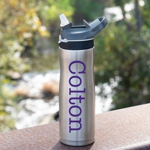 May include: A silver water bottle with a black lid and a purple name "Colton" on the side.