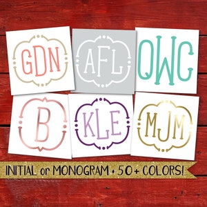 May include: Six different monogram decals with various colors and letter combinations. The decals are on a red wood background. The text below the decals reads "INITIAL or MONOGRAM. 50+ COLORS!"
