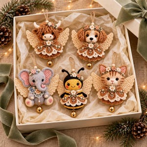 May include: Five crocheted animal ornaments in a gift box, including a highland cow, a spaniel, an elephant, a bee, and a tabby cat. Each figure features cream-colored crocheted wings, floral accents, and a small gold bell hanging from the base.