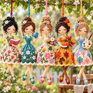 Könnte beinhalten: Fünf gehäkelte Puppen, die an Schnüren hängen, jede mit einem einzigartigen Outfit und Accessoire. Eine hält ein rosa Buch, eine einen blauen Vogel, eine einen Blumenstrauß, eine einen Kürbis mit Herbstblättern und eine eine Malerpalette.