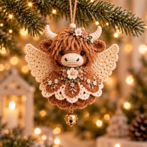 May include: A crocheted Highland cow ornament featuring a brown body, cream-colored wings, and a floral crown. The cow has a textured mane, small horns, and a white flower accent on its chest. A small gold-toned metal bell hangs from the bottom.