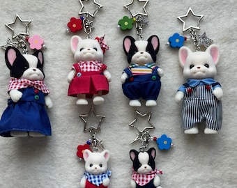 May include: Set of six adorable plush dog keychains. The dogs are black and white with different colored outfits. Each keychain features a star charm and colorful beads.