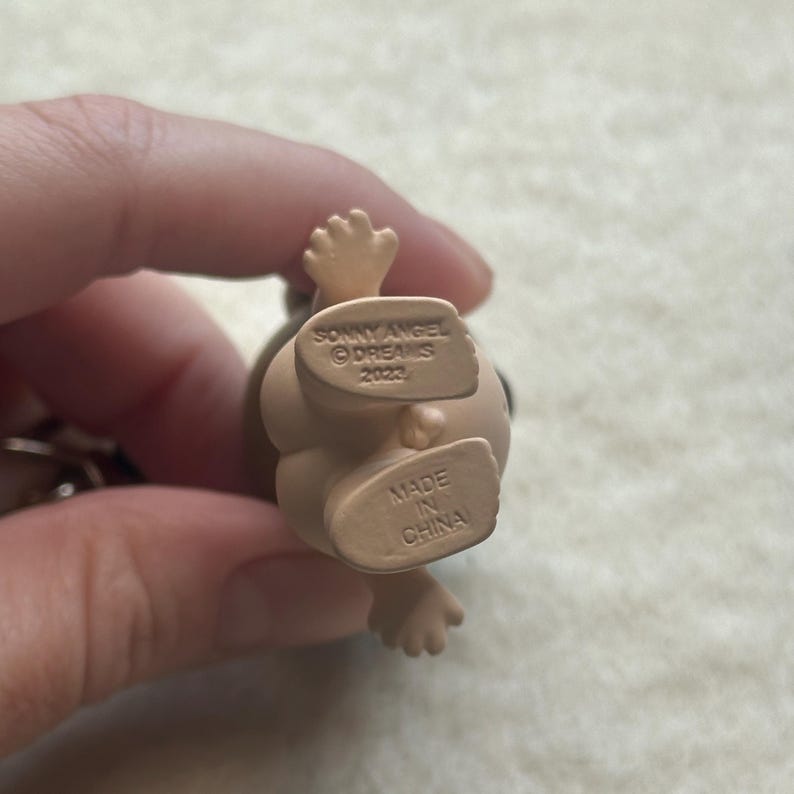May include: A small, tan figurine with a rounded body and tiny arms and legs. The figurine's underside features the text "SONNY ANGEL &copy;DREAMS 2022" and "MADE IN CHINA".