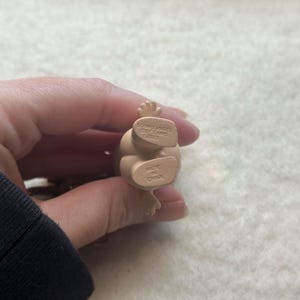 May include: A small, beige Sonny Angel figurine. The bottom of the figurine has the text "SONNY ANGEL DREAMS 2023" and "MADE IN CHINA". The figurine is held in a person's hand.