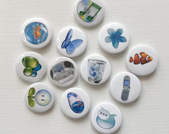 May include: A collection of twelve circular pin-back buttons featuring various illustrations including a goldfish in a bowl, a blue butterfly, a flower, a clownfish, a CD with a musical note, a boombox, a trash can, a flip phone, and a computer mouse.