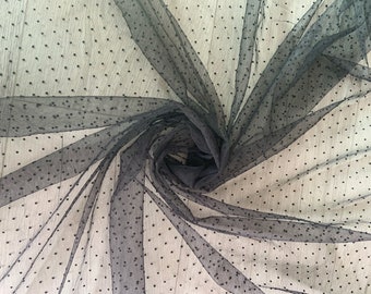 May include: Black tulle fabric with small black polka dots. The fabric is folded and arranged in a spiral pattern.