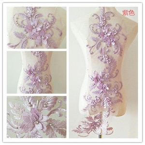 Könnte beinhalten: Eine zarte Applikation aus lila Spitze mit floralen Mustern und Perlenakzenten. Die Applikation ist perfekt, um Kleidung, Accessoires oder Wohnaccessoires einen Hauch von Eleganz zu verleihen.