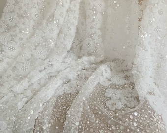 May include: White floral lace fabric with sequins and pearls. The fabric is sheer and delicate, with a soft, flowing texture.