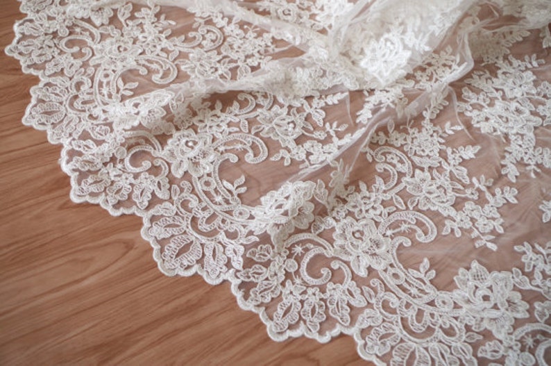 May include: White lace fabric with a delicate floral pattern. The lace is sheer and has a soft, flowing texture.