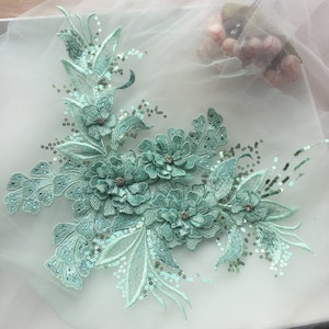 May include: A light green floral applique with sequins. The applique features several flowers and leaves.