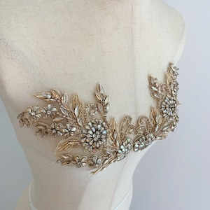 Op de afbeelding: Gouden parel applicatie met heldere, iriserende stenen en een bloemmotief.