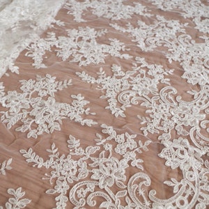 May include: White lace fabric with a delicate floral pattern. The lace is made of a sheer mesh with intricate embroidery.