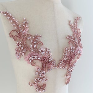 以下が含まれることがあります： ラインストーンとビーズをあしらった、繊細なピンクの花のアップリケ。どんな衣服にも輝きを加えるのに最適です。