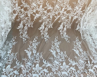 May include: White lace fabric with a floral and paisley design. The delicate lace features intricate patterns of flowers, leaves, and swirling motifs. The fabric is semi-sheer, with a scalloped edge along the bottom. Ideal for bridal wear or decorative projects.