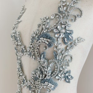 May include: A silver and blue beaded applique with a floral design. The applique is made of rhinestones and beads, and it is perfect for adding a touch of sparkle to any garment.