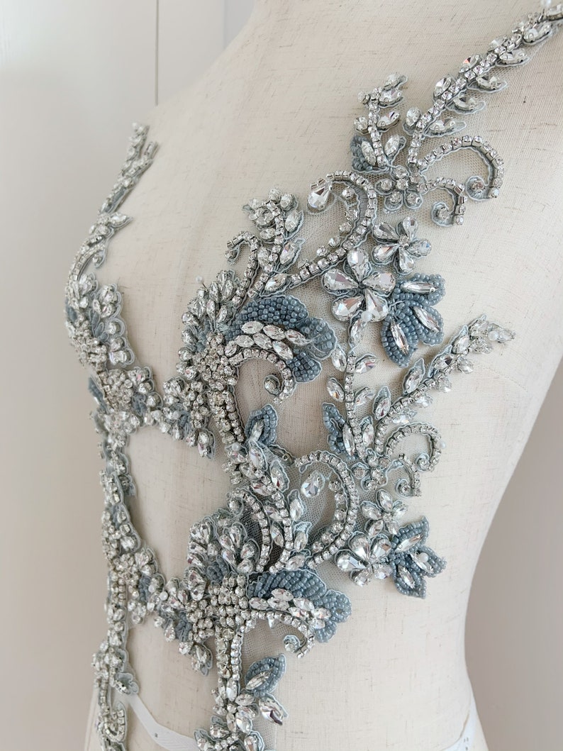 May include: A silver and blue beaded applique with a floral design. The applique is made of rhinestones and beads, and it is perfect for adding a touch of sparkle to any garment.