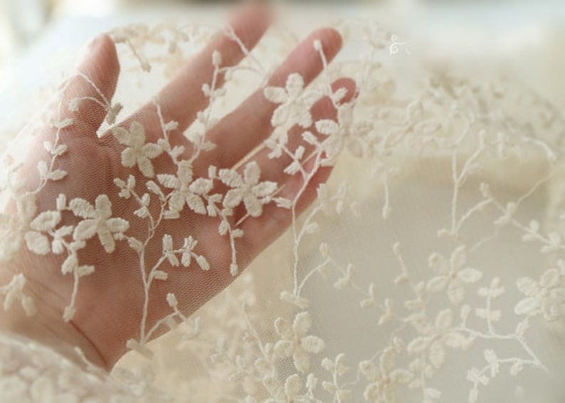 May include: Ivory lace fabric with a delicate floral pattern. The lace is sheer and has a soft, romantic feel.