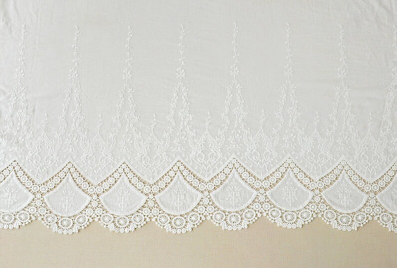 May include: White cotton lace trim with a scalloped edge and delicate floral embroidery. The lace has a repeating pattern of small flowers and leaves.