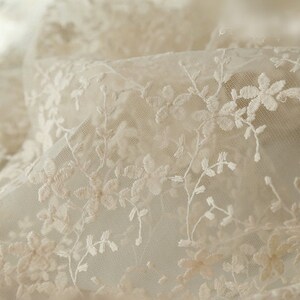 May include: Close-up of delicate white lace fabric with a floral pattern. The lace is sheer and has a soft, romantic feel.