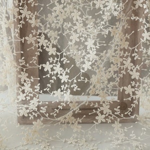 May include: Ivory floral lace fabric with a delicate pattern of small flowers and branches. The lace is sheer and has a soft, romantic feel.
