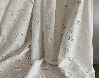 May include: White cotton fabric with a delicate, embroidered sunflower pattern. The fabric has a scalloped edge and is perfect for crafting projects.
