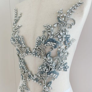 May include: A silver and blue beaded and rhinestone applique with a floral design. The applique is perfect for adding a touch of sparkle to any garment.