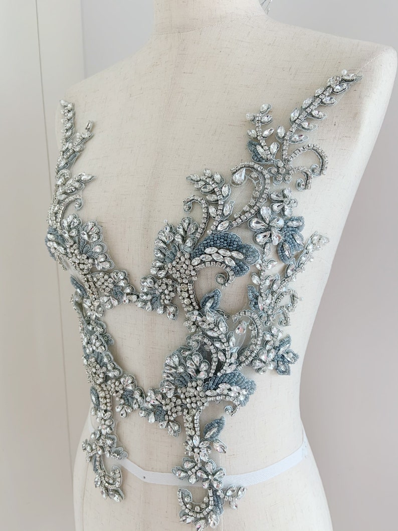 May include: A silver and blue beaded and rhinestone applique with a floral design. The applique is perfect for adding a touch of sparkle to any garment.