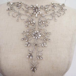 May include: A silver rhinestone applique with a floral design. The applique is ideal for adding a touch of sparkle to any garment.