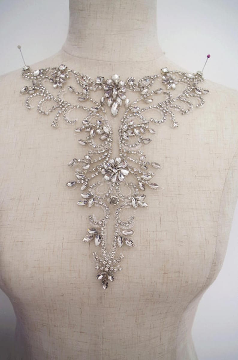 May include: A silver rhinestone applique with a floral design. The applique is ideal for adding a touch of sparkle to any garment.