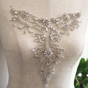 May include: A silver rhinestone applique with a floral design. The applique is ideal for adding a touch of sparkle to any garment.
