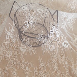 May include: White lace fabric with a delicate floral pattern. The fabric is draped over a wire basket.
