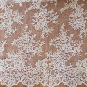 May include: White lace fabric with a delicate floral pattern. The lace is sheer and has a soft, flowing texture.