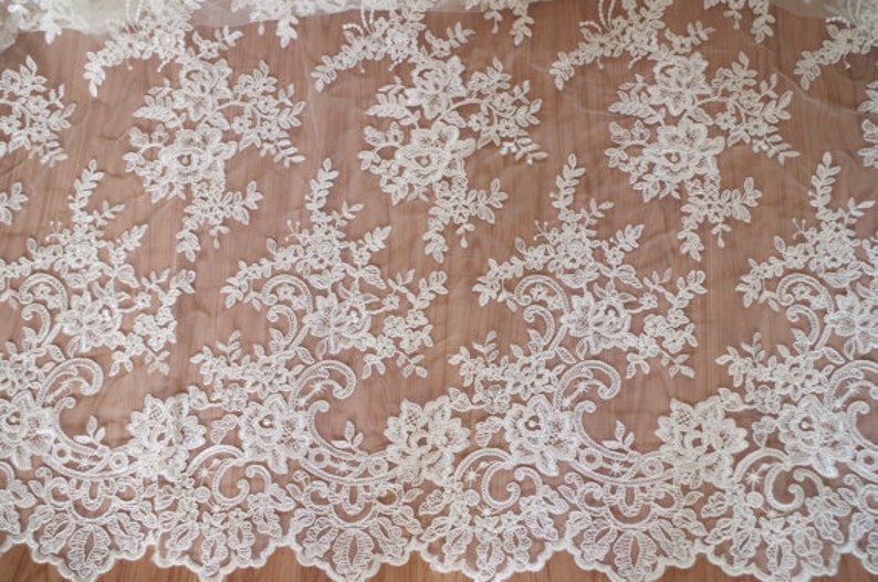 May include: White lace fabric with a delicate floral pattern. The lace is sheer and has a soft, flowing texture.