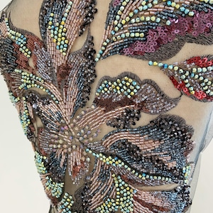 Puede incluir: Una tela de malla negra transparente con un intrincado patrón de bordado floral. El diseño está densamente adornado con lentejuelas iridiscentes, cuentas de canutillo metálicas y cristales facetados en tonos bronce, rojo y azul verdoso.