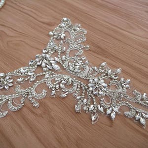 May include: A silver beaded and sequined applique with a floral design. The applique is on a sheer fabric background.