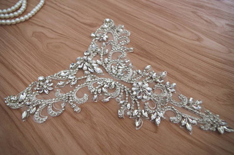 May include: A silver beaded and sequined applique with a floral design. The applique is on a sheer fabric background.