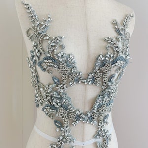 May include: A delicate, silver and blue beaded applique with a floral design. The applique is perfect for adding a touch of sparkle to any garment.