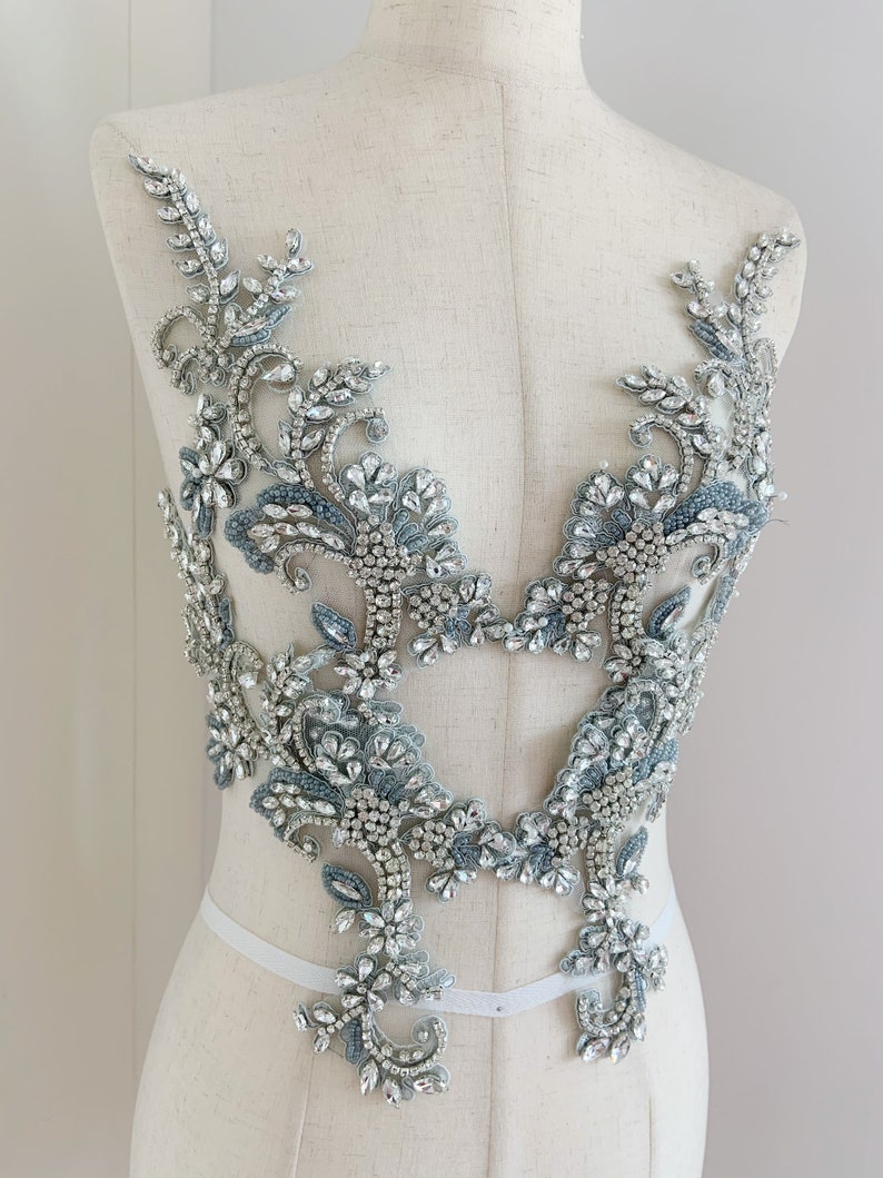 May include: A delicate, silver and blue beaded applique with a floral design. The applique is perfect for adding a touch of sparkle to any garment.