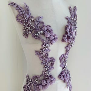May include: Lavender floral applique with beaded and sequined details. The applique features a variety of floral and leaf designs, with clusters of small, round beads and larger, sparkling sequins. Designed to be sewn onto fabric.