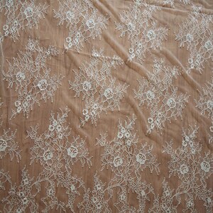 May include: White floral lace fabric with a delicate pattern. The lace is sheer and has a soft, flowing texture.