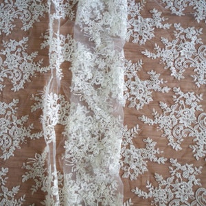 May include: White lace fabric with a delicate floral pattern. The lace is sheer and has a soft, flowing texture.