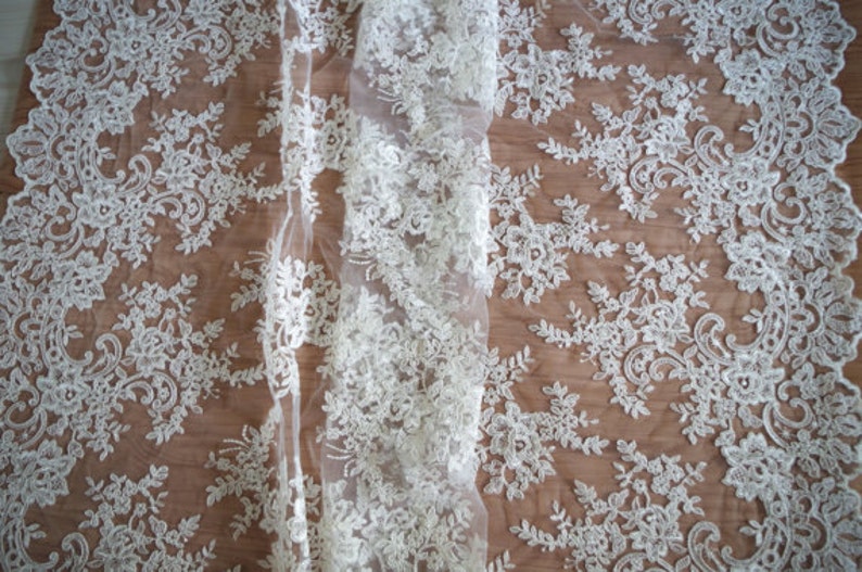 May include: White lace fabric with a delicate floral pattern. The lace is sheer and has a soft, flowing texture.