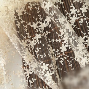 May include: Close-up of ivory lace fabric with a delicate floral pattern. The lace is sheer and has a soft, romantic feel.